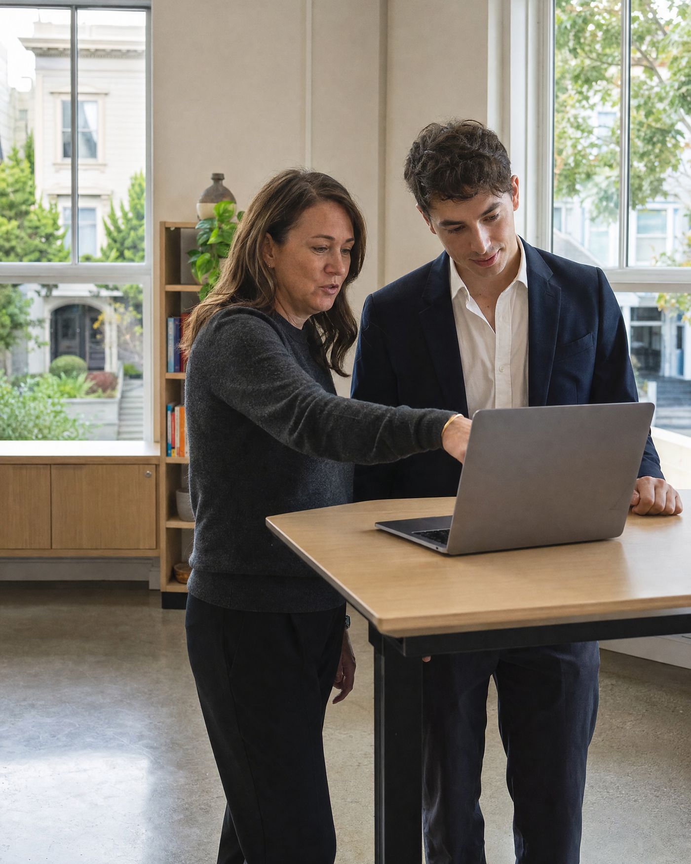 A manager walks a new hire through his first week at a standing desk in a bright open office